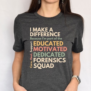 Könnte beinhalten: Ein dunkelgraues T-Shirt mit dem Text "I make a difference because I'm part of the Educated, Motivated, Dedicated, Forensics Squad" in bunten Farben.