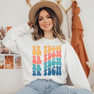 Op de afbeelding: Wit sweatshirt met een kleurrijk retro-ontwerp met de tekst "ER TECH" die vier keer wordt herhaald.