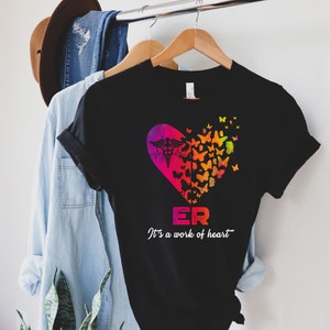 May include: Black t-shirt with a colorful heart design featuring a medical symbol and butterflies. The text "ER It's a work of heart" is printed below the heart.
