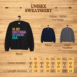 May include: Black, navy, and dark heather unisex sweatshirt with the text "In My Doctoral Student Era" in rainbow colors. Size chart with chest and length measurements in inches.