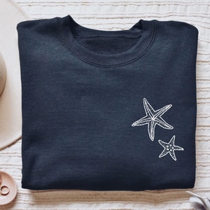 May include: A dark blue sweatshirt with a white embroidered design of two starfish on the front.