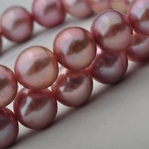 Może przedstawiać: Sznur różowych pereł słodkowodnych. Perły są okrągłe i mają gładkie, błyszczące wykończenie.