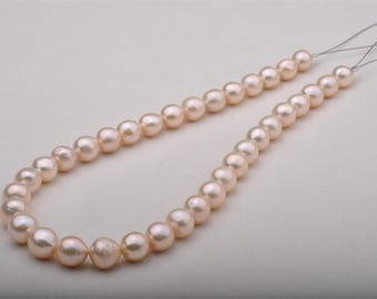 May include: A strand of light pink pearls, strung on a thin, nearly invisible thread. The pearls are round and have a subtle luster, creating a classic and elegant look. The necklace is displayed against a plain, light background.