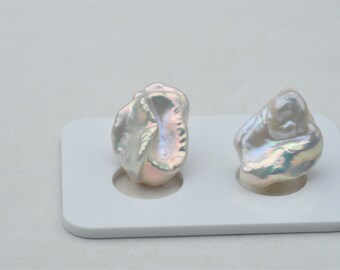 May include: Two iridescent white baroque pearls on a white display stand. The pearls are irregular in shape and have a pearlescent sheen.