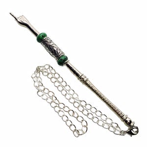 May include: A silver-colored metal yerba mate bombilla with a hand-shaped filter and green stone accents. The bombilla has a textured handle and is attached to a silver chain.