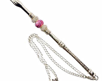 May include: A silver-colored hookah pipe with a decorative design, a pink and purple stone, and a chain. The pipe has a detailed pattern and a star-shaped charm at the end of the chain.
