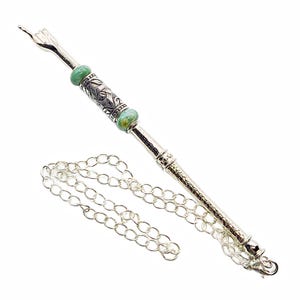 May include: A silver-toned metal accessory with a chain, featuring a decorative design with green beads. The top has a hand-shaped detail. The chain is made of small, linked circles.
