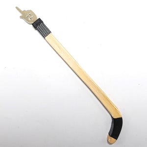 May include: A wooden hockey stick with a black blade and a silver hand pointing upwards at the top. The hand has a black band around the wrist.