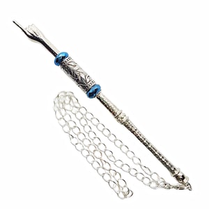 May include: A silver-toned metal tool with a decorative handle, blue crystal accents, and a chain. The tool has a pointed end and a detailed design on the handle. The chain is made of small, linked circles.