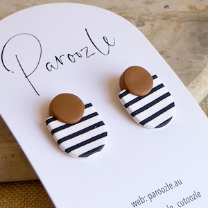 Op de afbeelding: Een paar zwart-wit gestreepte oorbellen met bruine cirkels erop. De oorbellen worden gepresenteerd op een witte kaart met het woord "Paroozle" erop. De kaart bevat ook de tekst "web: paroozle.au" en "insta: paroozle_cutoozle".