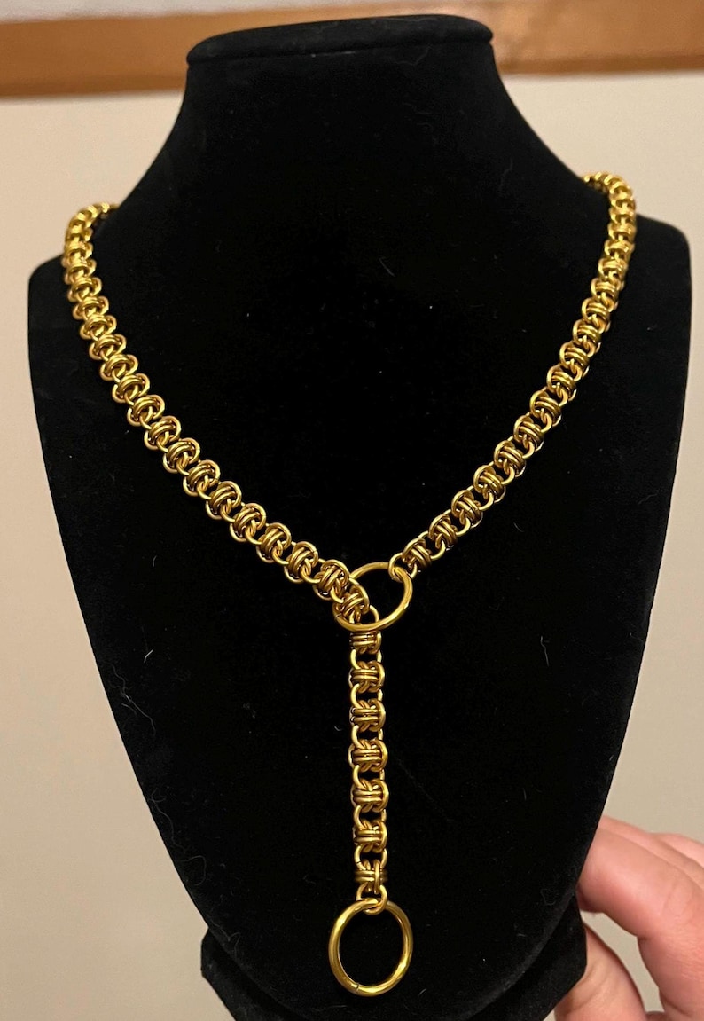 K&ouml;nnte beinhalten: Eine goldene Kettenkette mit Y-f&ouml;rmigem Design und zwei runden Verschl&uuml;ssen. Die Kette wird auf einer schwarzen Puppe pr&auml;sentiert.
