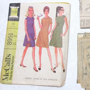 May include: Vintage McCall's sewing pattern for Misses' dress in two versions. The pattern envelope features illustrations of the dresses in purple, orange, and green. Includes pattern pieces and instructions. The pattern number is 8951.