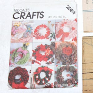 May include: A collection of craft patterns, including a McCall's Crafts pattern booklet with images of wreaths. Additional patterns feature a jack-o'-lantern and bear illustration. The patterns are on a white surface.