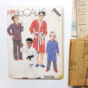 May include: A vintage sewing pattern for children's pajamas and robes. The pattern is from McCall's and is number 2054. The pattern includes instructions for making a plaid pajama set, a red robe, and a blue robe.