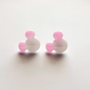 May include: A pair of pink and white glitter mouse ear stud earrings.