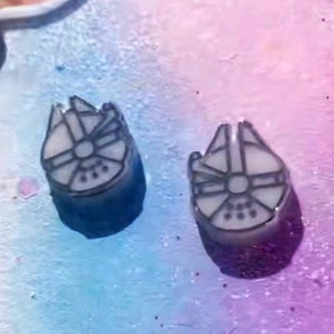 May include: A pair of white resin earrings with a black outline of the Millennium Falcon spaceship from Star Wars.