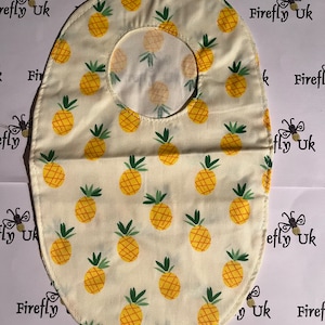 Könnte beinhalten: Ein weißer Stofflätzchen mit einem Ananas-Muster. Das Lätzchen hat ein Loch in der Mitte für den Hals.