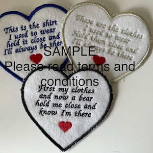 May include: Three white felt heart-shaped patches with black stitching around the edges. The patches have embroidered text that reads: "This is the shirt I used to wear hold it close and I'll always be there", "These are the clothes I used to wear Hold them close and I'll always be there", and "First my clothes and now a bear hold me close and know I'm there".
