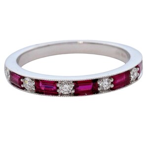 May include: A silver ring featuring alternating rectangular red gemstones and round white gemstones. The ring has a delicate, textured border and is set against a white background. The gemstones are evenly spaced around the band.