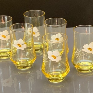 Puede incluir: Juego de seis vasos de vidrio amarillo con diseños florales blancos. Cada vaso presenta una sola flor blanca con un centro amarillo.