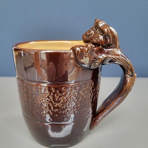 May include: A brown ceramic mug with a textured surface and a sculpted squirrel handle.