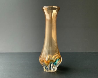 May include: A clear glass vase with a textured, amber-colored body and a swirling, multi-colored design at the base. The design features shades of blue, green, and gold.