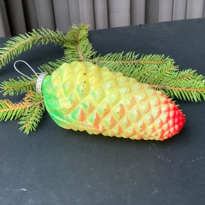 Könnte beinhalten: Ein grüner, gelber und roter gläserner Weihnachtsbaumschmuck in Form einer Tannenzapfen.