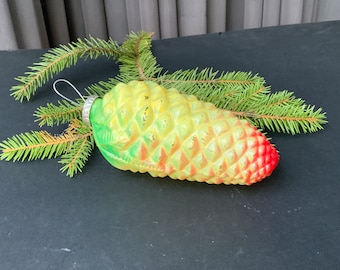 May include: A green, yellow, and red glass Christmas ornament shaped like a pine cone.