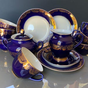 Puede incluir: Un juego de té completo en azul cobalto con detalles de filigrana dorada. El juego incluye tazas, platillos, cuencos, platos, una tetera y una jarra de crema. Los platos tienen un centro blanco con un borde azul y dorado. Un juego de té lujoso y elegante.
