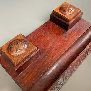 May include: A vintage wooden desk set with a rich, reddish-brown finish. The set includes a rectangular base with a pen tray and two square boxes with carved circular designs on top. The wood grain is visible.