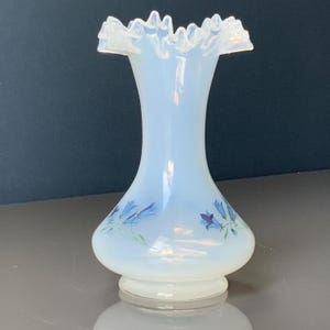 May include: An opalescent glass vase with a frilled rim and a rounded base. The vase has a floral pattern in blue and green. The vase is about 20 cm tall. A decorative item for the home.