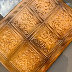 May include: A brown leather notebook cover with a decorative embossed pattern. The cover has a border of small lines around the edges.