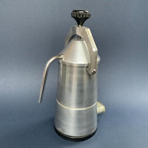 Puede incluir: Una cafetera de espresso de aluminio plateado con una perilla negra en la parte superior. La cafetera tiene un pico para verter el café.