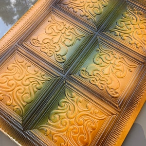 May include: A decorative tray with a raised, embossed design. The tray is made of a dark brown material and has a gold-colored finish. The design features a repeating pattern of swirls and leaves.