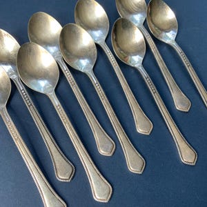 Può includere: Un set di cucchiai d'argento disposti diagonalmente su una superficie blu scuro. I cucchiai hanno coppette ovali e manici decorati. I cucchiai sono probabilmente vintage o antichi e sono adatti per servire.