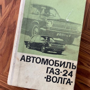 May include: A vintage book cover featuring a black and white image of a GAZ-24 Volga car. The title of the book is "Автомобиль ГАЗ-24 •ВОЛГА•".