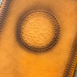 May include: A tan leather-bound journal with a decorative embossed design of a city skyline on the front cover.
