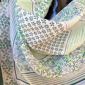 Può includere: Un foulard di seta bianco e verde con un motivo floreale. Il foulard ha un bordo verde e uno sfondo bianco con fiori verdi.