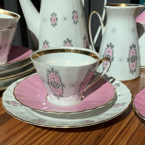 K&ouml;nnte beinhalten: Vintage Teeservice mit wei&szlig;en Porzellantassen, Untertassen und Servierteilen. Das Set hat ein rosa-schwarzes Dekor mit goldenen Verzierungen. Enth&auml;lt Tassen, Untertassen, eine Teekanne, einen Sahnek&auml;nnchen und eine Zuckerdose.