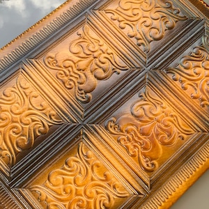 May include: A brown leather journal with a decorative embossed pattern. The journal has a dark brown border and a gold-colored embossed design.