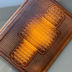 May include: A brown leather journal with a decorative embossed pattern of repeating circles and a geometric design. The journal has a stitched border.