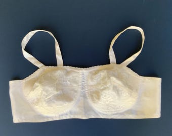 May include: Ivory-colored bra with lace detailing on the cups and satin straps. The bra has a classic design with a scalloped edge along the top and a smooth, solid fabric on the sides.