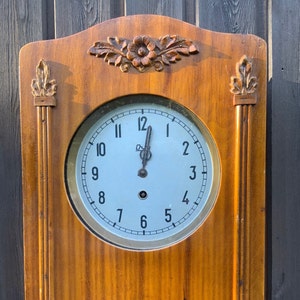 May include: A wooden wall clock with a white face and black hands. The clock has Roman numerals and a decorative floral design on the top.