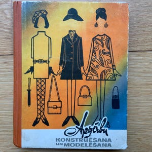 May include: A vintage book cover with a yellow, orange, and red background. The cover features a black and white illustration of three figures wearing different outfits and accessories. The book title is "Apģērbu Konstruēšana un Modelēšana".