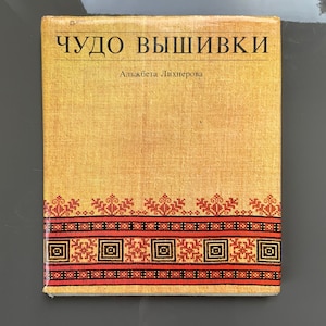 Puede incluir: Un libro amarillo con el título "Чудо вышивки" y el autor "Альжбета Лихнерова" en la portada. La portada tiene un borde bordado rojo y negro.