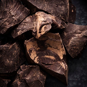 Puede incluir: Primer plano de trozos de chocolate marr&oacute;n oscuro sobre una superficie negra. El chocolate tiene una textura rugosa y rota.