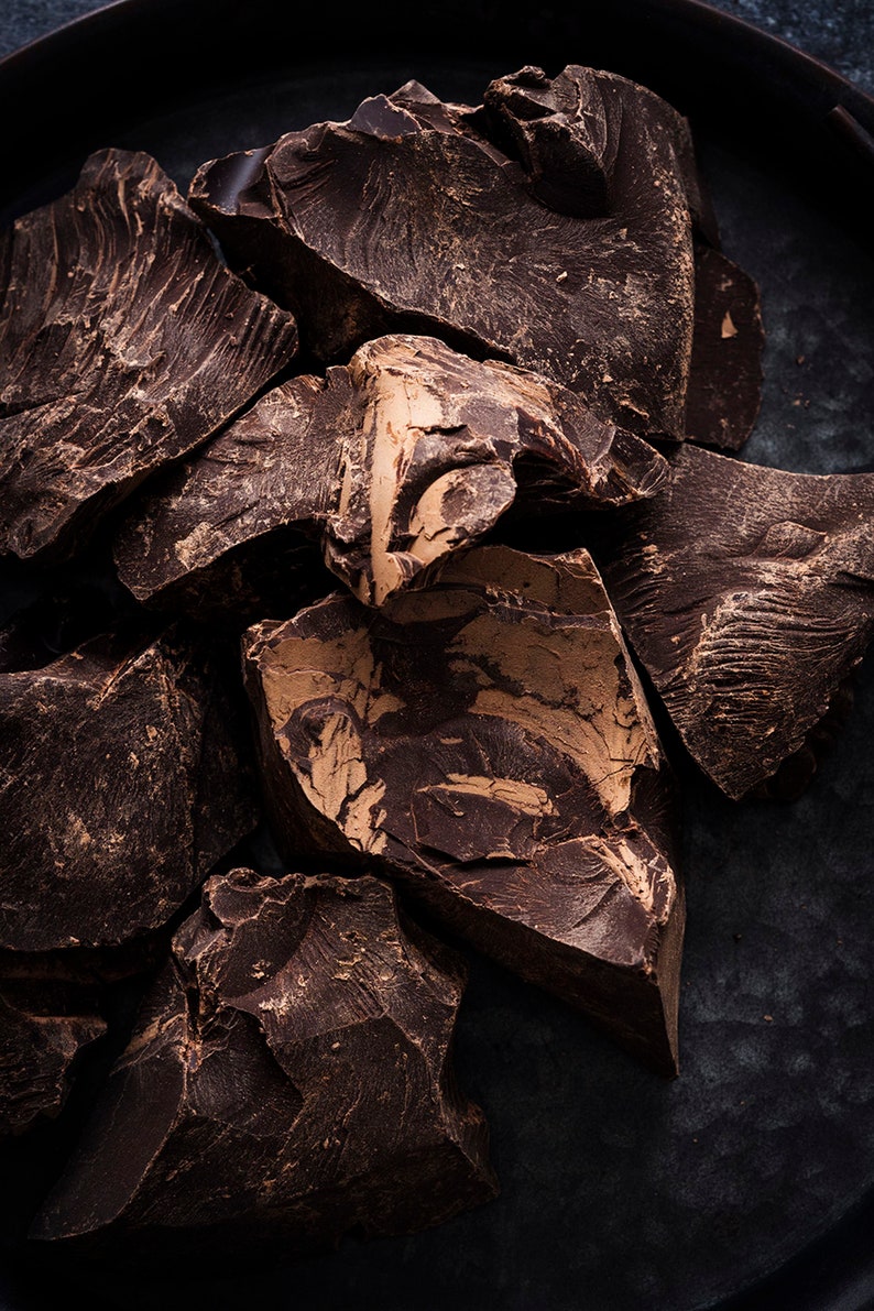 Puede incluir: Primer plano de trozos de chocolate marr&oacute;n oscuro sobre una superficie negra. El chocolate tiene una textura rugosa y rota.