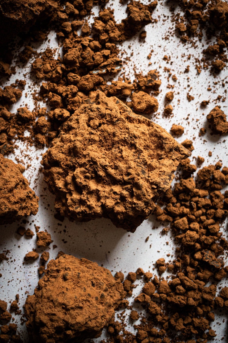 Puede incluir: Primer plano de un mont&oacute;n de polvo de cacao marr&oacute;n sobre una superficie blanca. El polvo es de varios tama&ntilde;os y formas, algunos est&aacute;n agrupados.