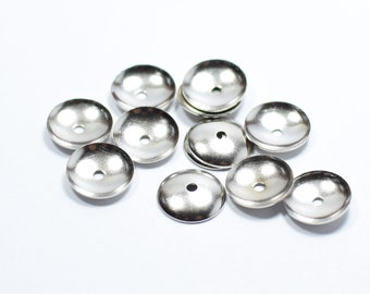 May include: A group of silver metal beads with a round, flat base and a raised, domed top. The beads have a small hole in the center for threading.