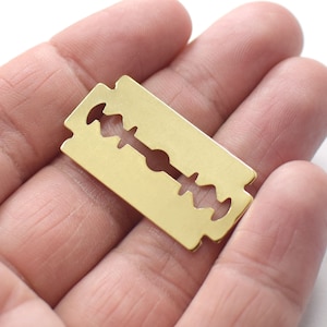 May include: A gold-colored metal razor blade with a sharp edge. The blade is held in a hand.